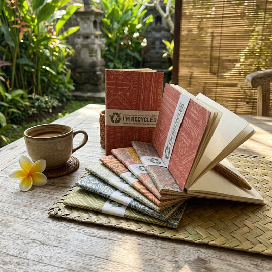 Assorted Balinese handmade recycled paper notebooks with patterned covers displayed in a tropical setting