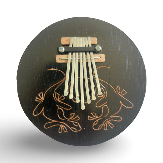 Front view of a handcrafted coconut shell kalimba featuring metal keys and an engraved gecko motif on the dark wooden surface