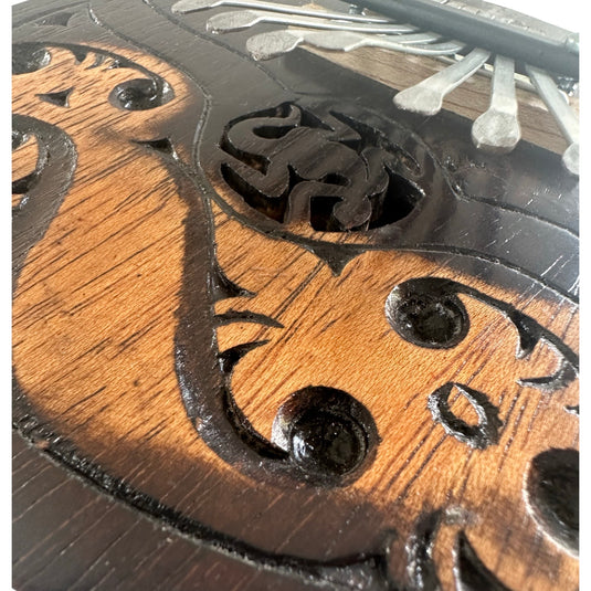 Close-up of the engraved Island Flow design on a handcrafted coconut shell kalimba, showing carved details and metal keys