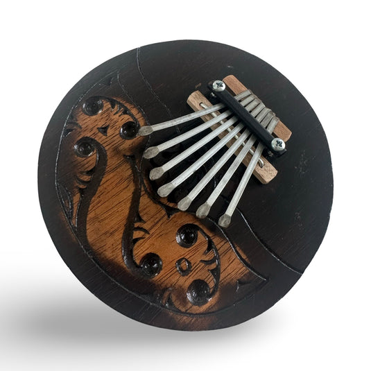Angled front view of a handcrafted coconut shell kalimba featuring metal keys and an engraved Island Flow pattern